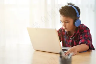 带着耳机坐在电脑前学习的儿童