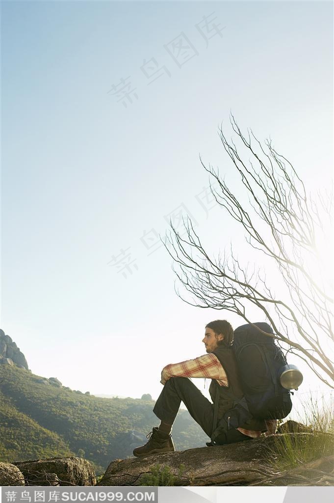 户外探险露营生活-背着背着坐在石头上向前眺望的外国男人