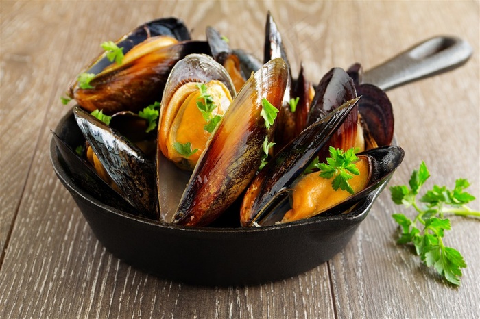 木桌上一盘烧熟的黑色贝壳高清图