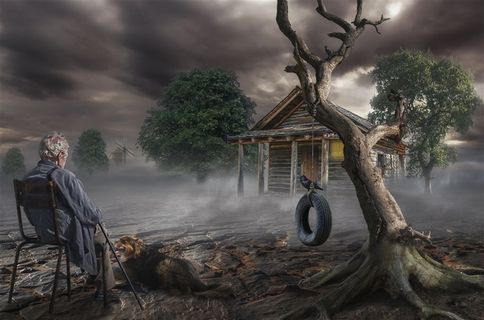 坐在贫瘠的大地上的老人和枯树木屋高清图片