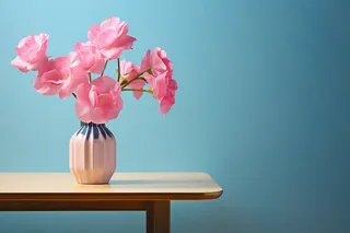 蓝色背景的粉色桌子上的花瓶里的粉色鲜花摄影图