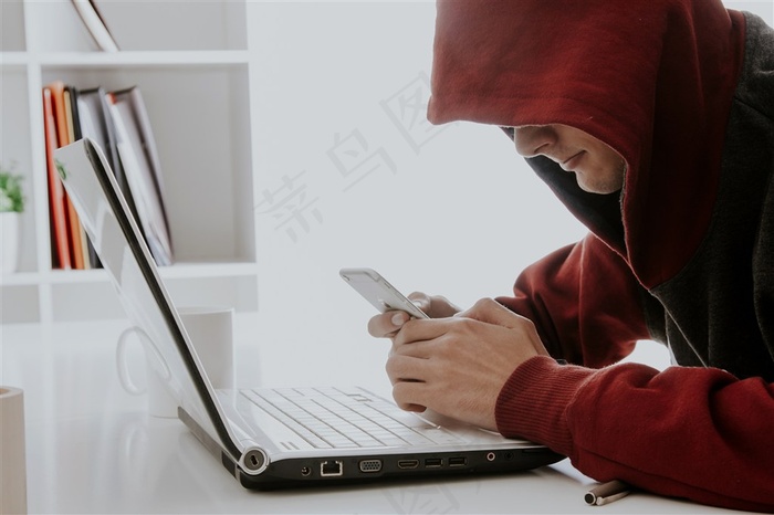 笔记本电脑前玩手机的男子