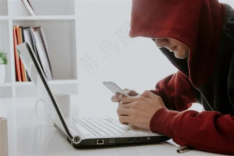 笔记本电脑前玩手机的男子 笔记本电脑前玩手机的男子