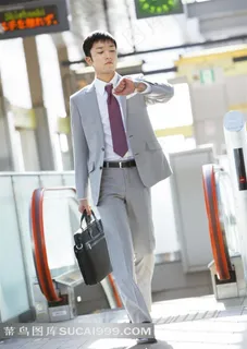 手拿公文包看手表向前走的商务男士图片