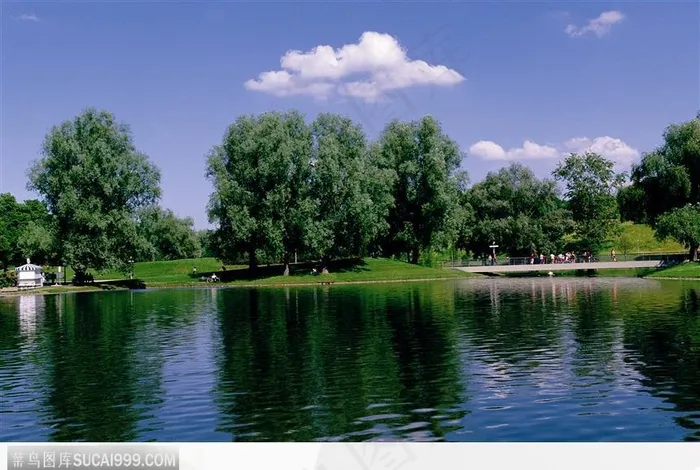 白云下的湖水、树木和桥上的游客