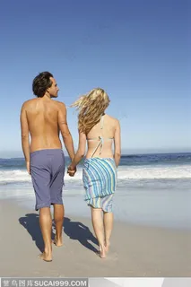 夫妻两手拉手在海边的沙滩上散步