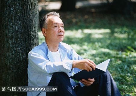 靠树木坐着看书的男老人素材