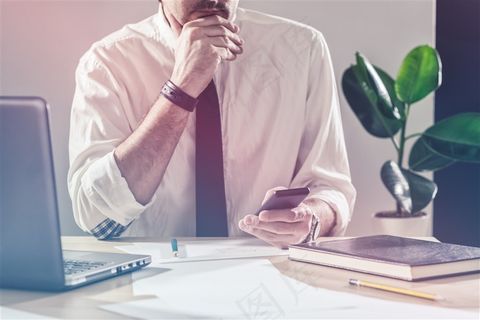 坐在办公桌前看手机的商务人士