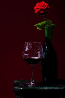 在红色玫瑰花旁边的红酒杯