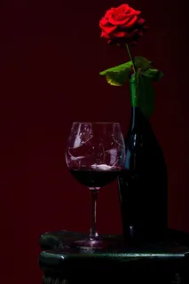 在红色玫瑰花旁边的红酒杯 在红色玫瑰花旁边的红酒杯