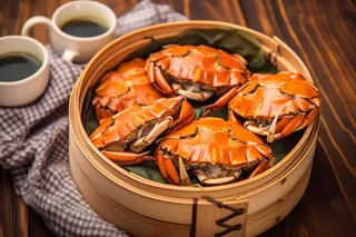 餐桌蒸笼屉里的螃蟹和茶壶摄影图