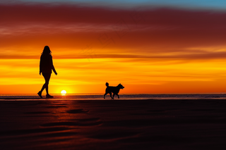 夕阳落日下遛狗的人海边沙滩晚霞摄影图