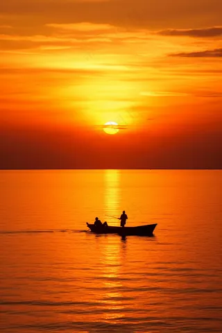 夕阳落日下的海洋湖面小船余晖倒影摄影图