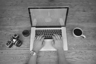 笔记本电脑上工作的人的黑白图像，相机和桌上的咖啡杯