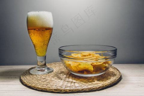 啤酒,酒杯,台灯,玻璃杯,啤酒杯,啤酒瓶和碗土豆片在桌子垫上